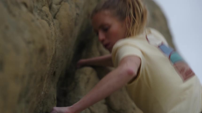 A woman is climbing the side of a mountain making sure the rocks she is holding are secure before she pulls herself up