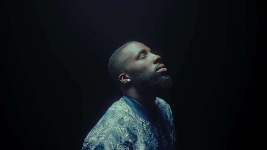 A light shines down on a man as he closes his eyes in a dark room