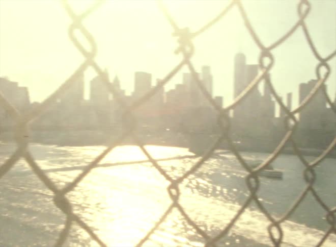 The brooklyn bridge and new york skyline in glaring sunshine through chain link