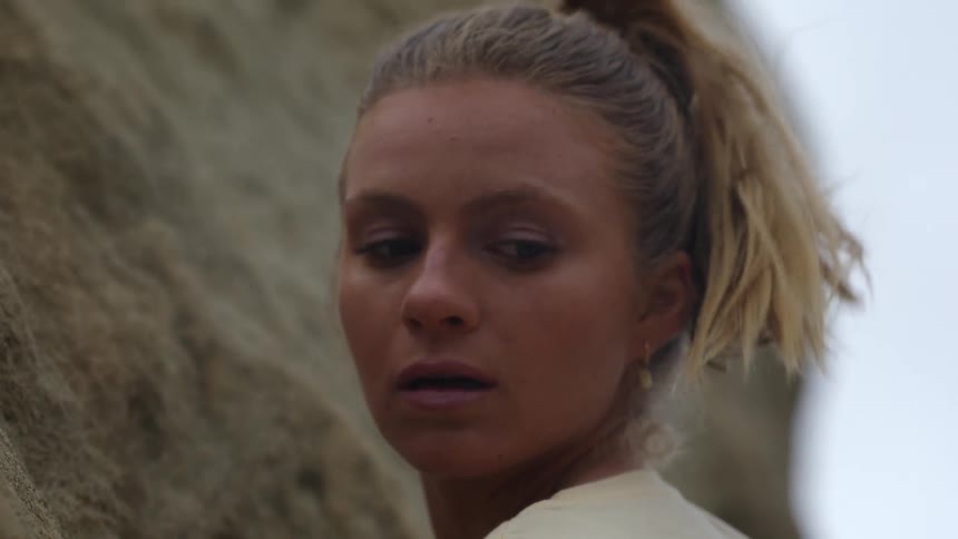 A woman up against a rock formation looks around as she considers her next move