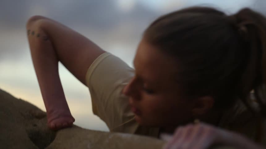 Blonde woman with one hand missing pulls herself up to the top of the rocks while rock climbing