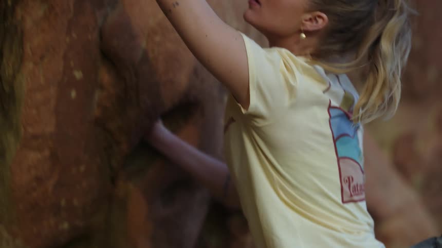 Blonde woman in a short sleeved shirt climbs up the rocks