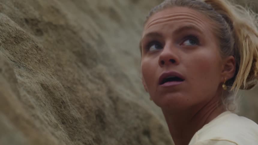 A woman climbing a rock pauses to check her foothold and look up