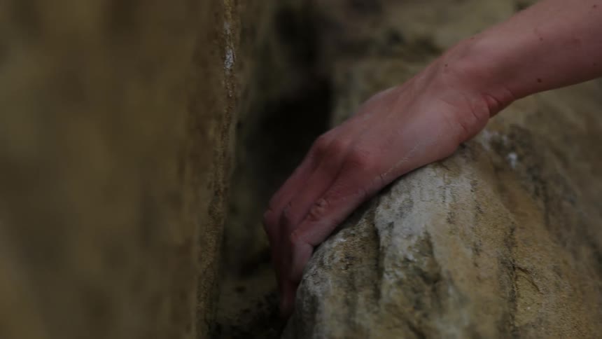 A rock climbers hand and fingers grasping a rock ledge then slipping off