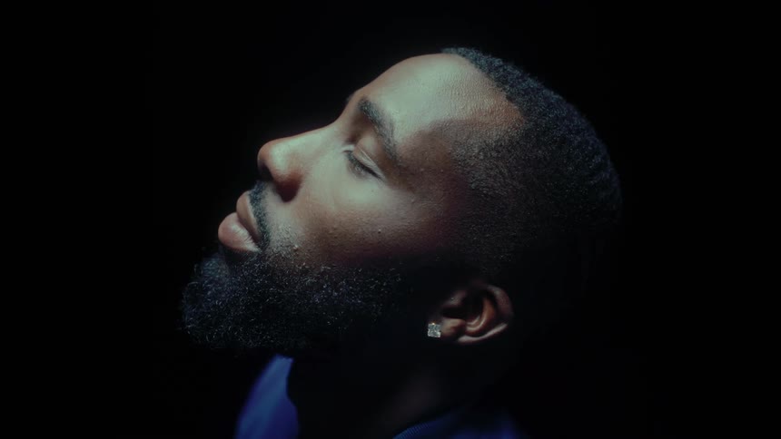 A young black man with his eyes closes raises his chin upwards and then lowers it