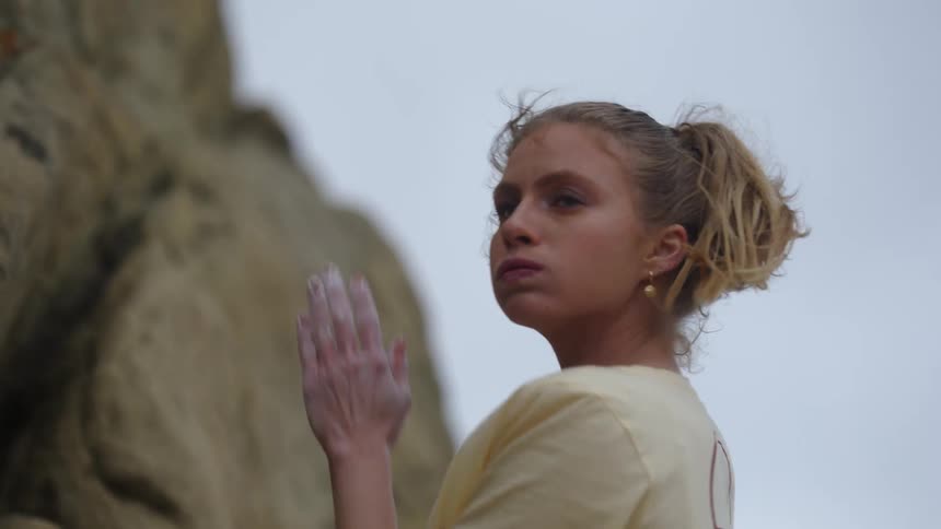 A woman rubs her palms with chalk exhales and gets ready to climb a rock on a breezy day