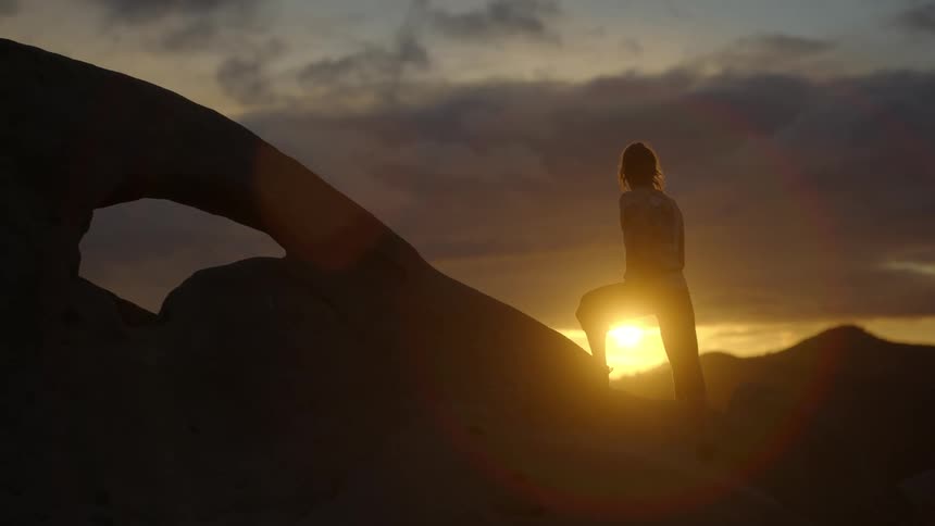 A woman climbs onto a rock formation to watch the sun set in a canyon