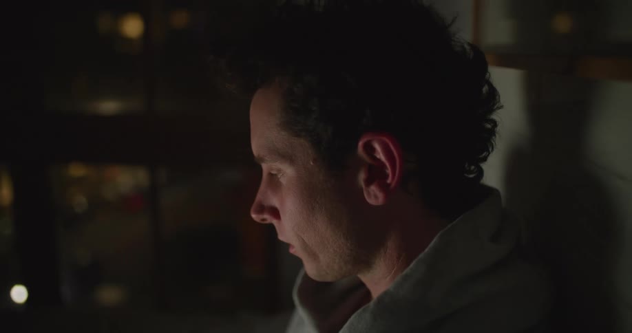 Man sits and looks out a window at cars passing by on the street below at night