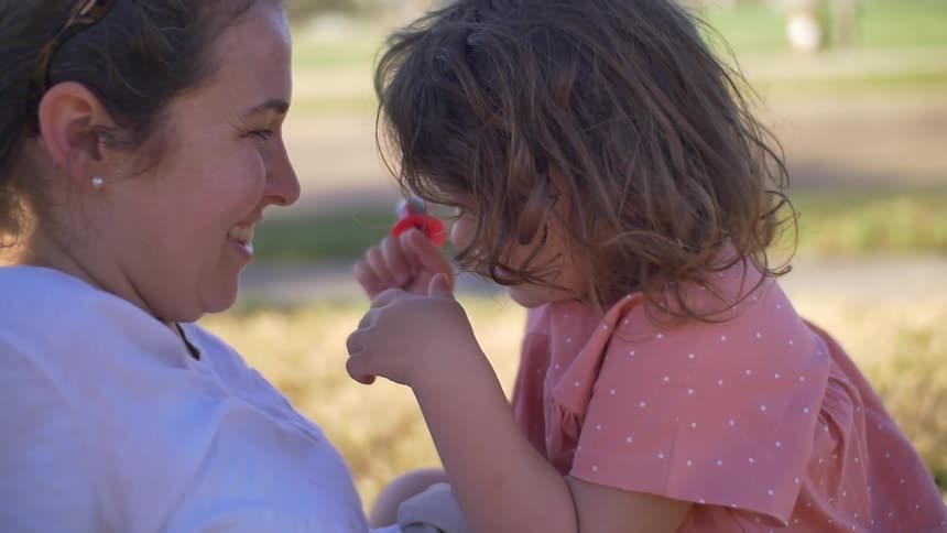 A woman and toddler girl are laughing and playing while sitting outside