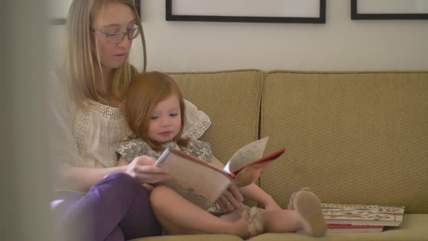 A woman and girl sit on the couch she is reading to her