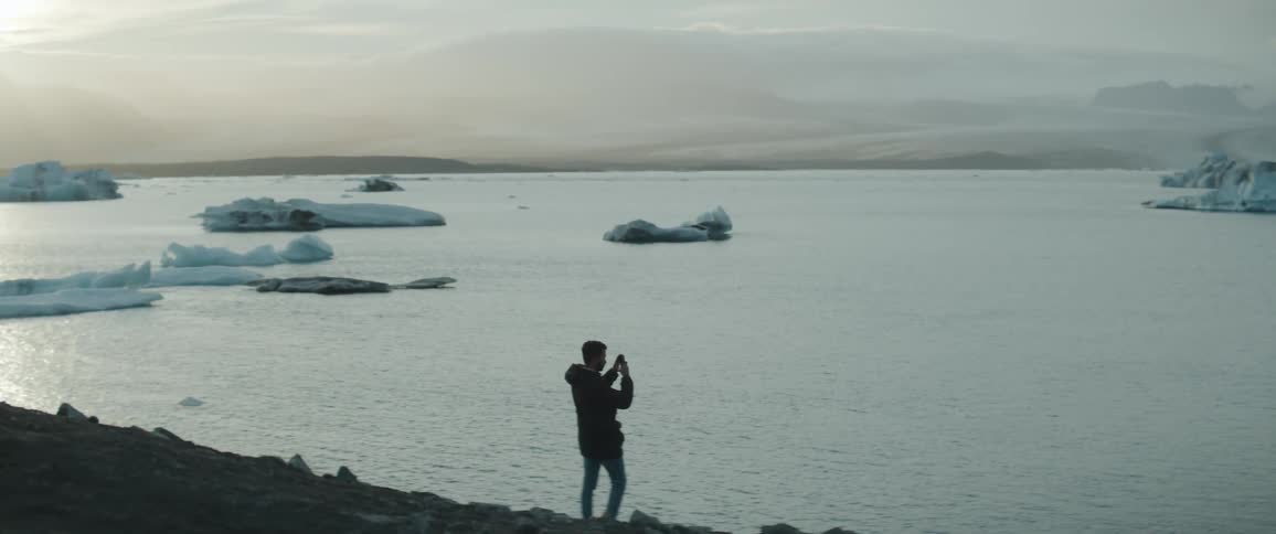 Silhouette of a man filming icebergs on the ocean with a phone at evening