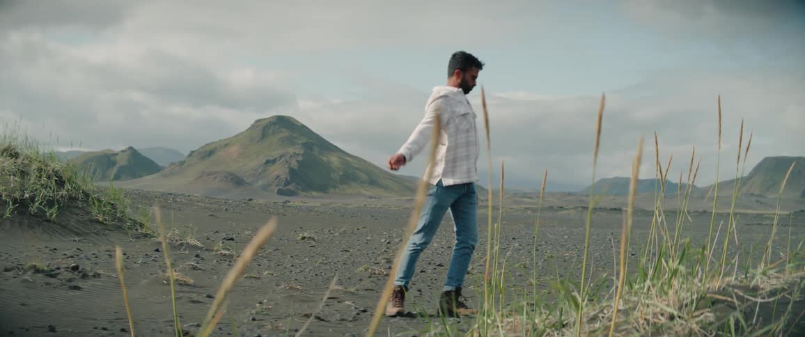 A man is outside doing a robotic dance with mountains in the distance