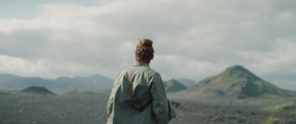 Man carrying a camera walks over the gravel on a deserted plain next to the mountains
