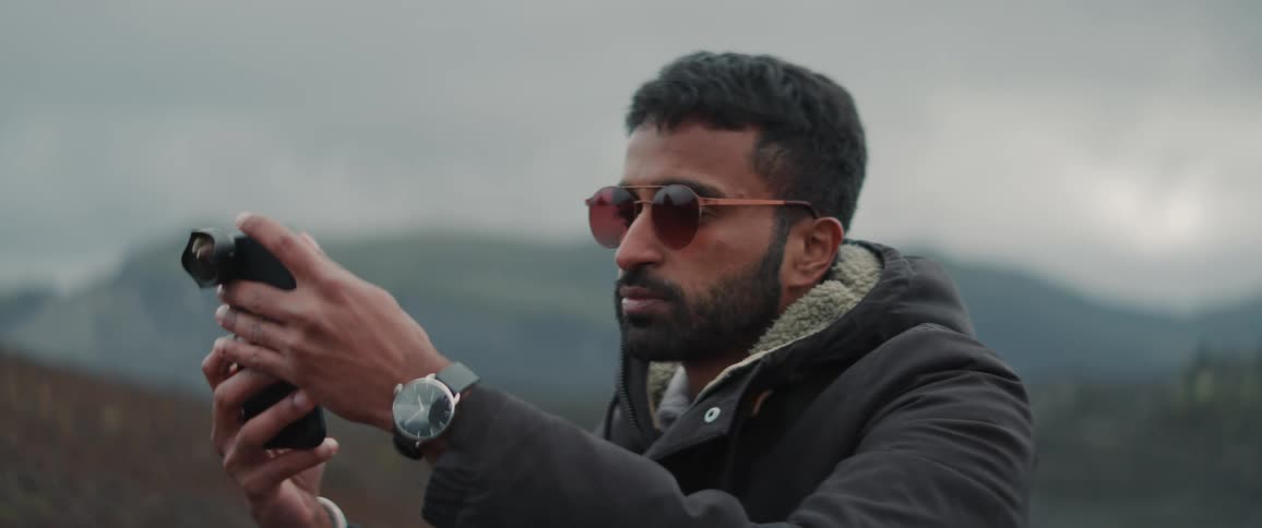 Young bearded man wearing sunglasses takes pictures with his phone using a special lens