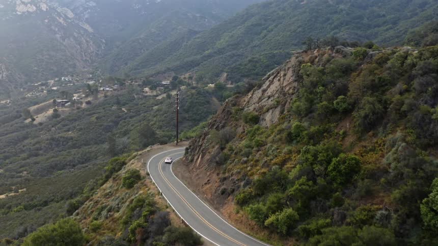 Aerial view of white car driving on mountain road taking a bend