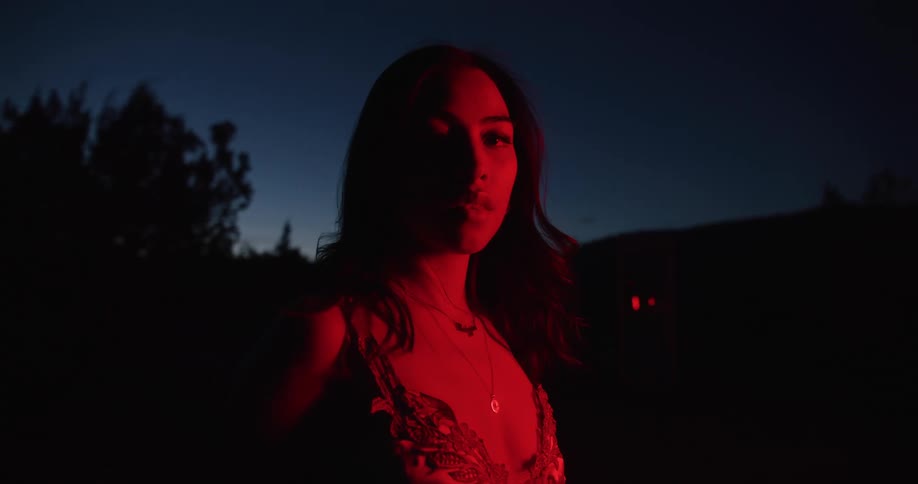 Silhouette of a young woman standing outdoors under red lights at night
