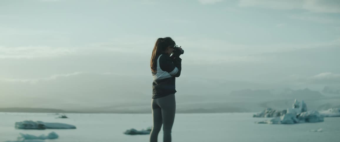 Young woman uses a camera to take pictures of icebergs floating on the ocean
