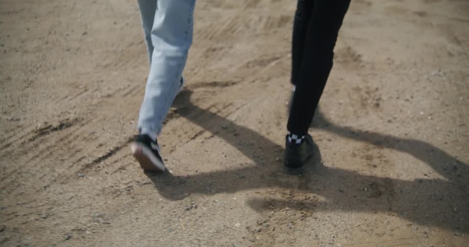 A couple are holding hands as they walk on a dirt road