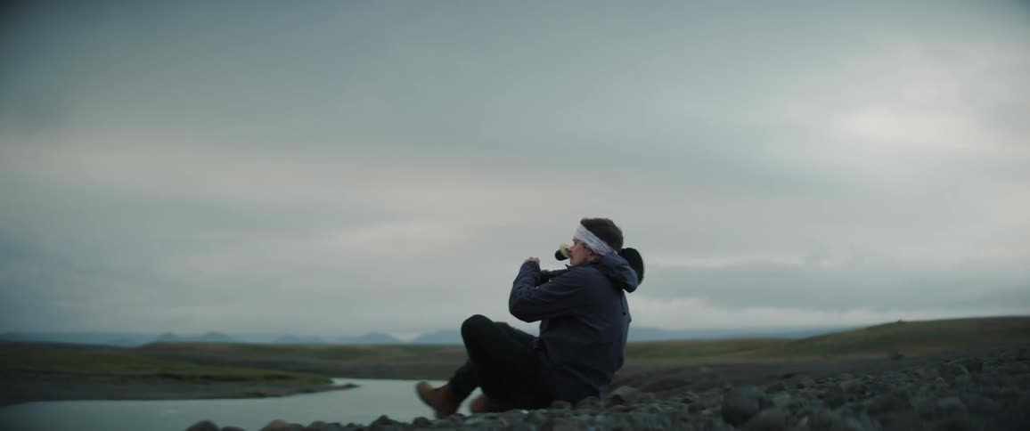 A man sits down at the edge of a creek with a large video camera