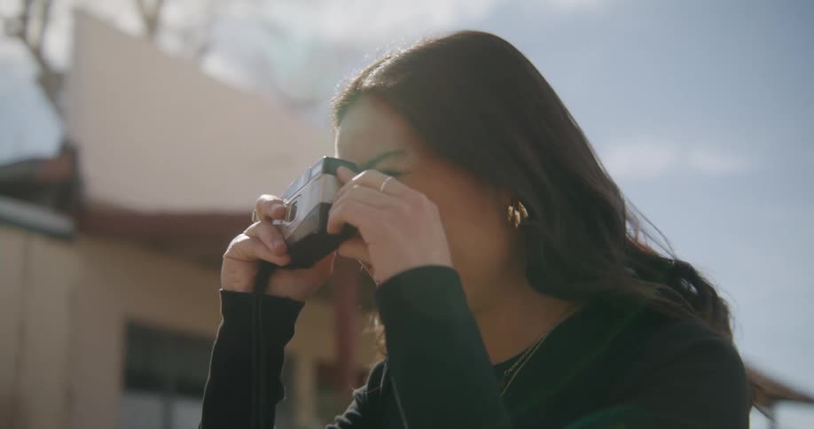 A woman is standing outside with a camera close to her face as she takes a picture
