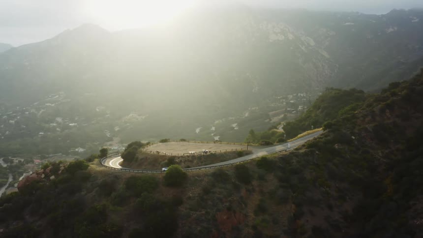 A car drives up a winding road on a mountain that rises above a small town