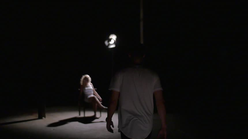 A man approaching a woman who is sitting under a stage lights in a dark room