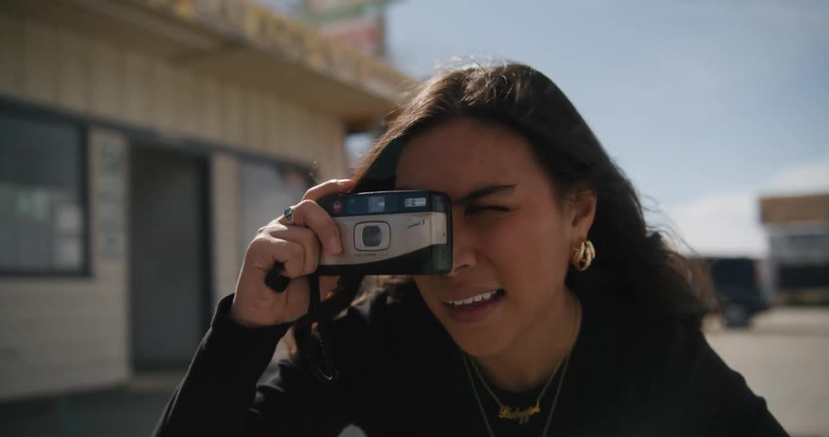 Close up of a young woman taking pictures with a small camera outside a roadside store