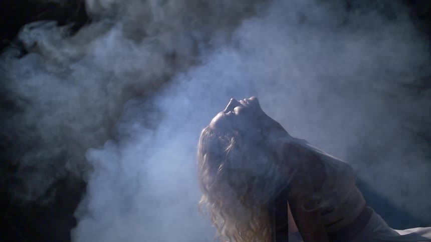 Smoke swirling around a woman as she leans backwards