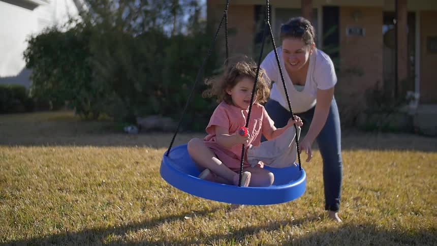 A woman pushes a girl on a swing