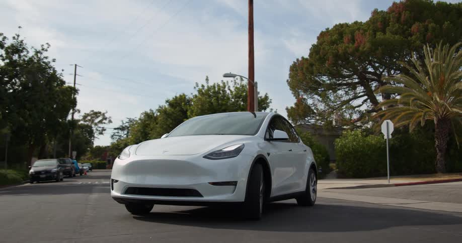 A white automobile has a turn signal blinking as it turns at an intersection