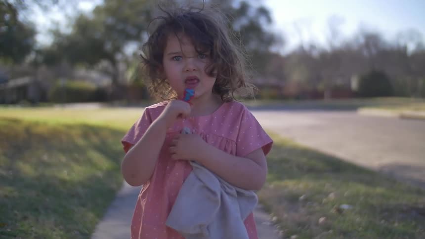 A girl licks her ring pop on the sidewalk