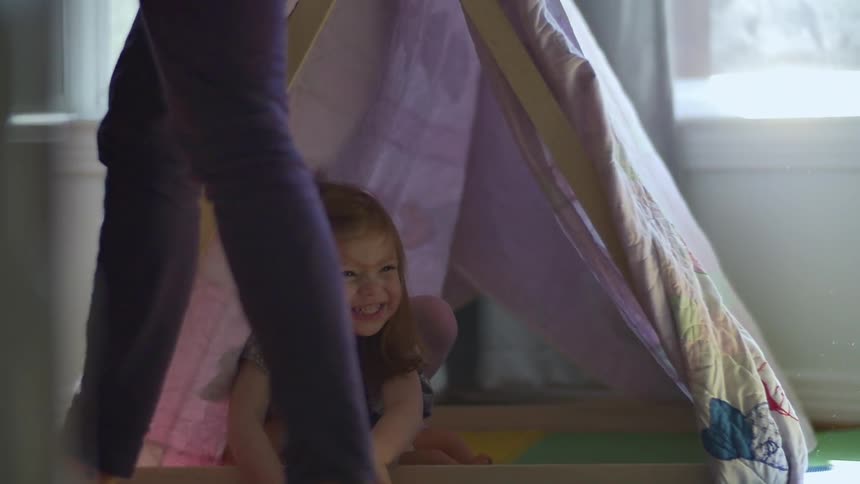 A child is in a blanket tent as a woman walks past