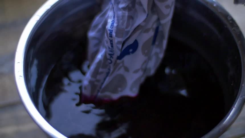 A piece of fabric is dipped in a bowl of dye