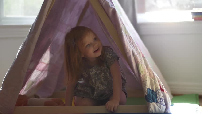 A toddler girl is  kneeling in a play tent and smiling
