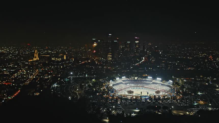 An aerial view of a city skyline and an arena with fireworks exploding in the night sky