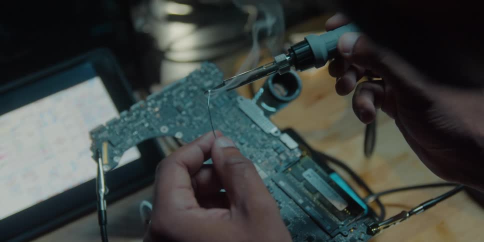 A man uses a soldering gun on wires on a circuit board