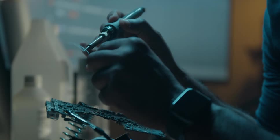 A man pulls some wire from a reel and uses a soldering iron while building a circuit board