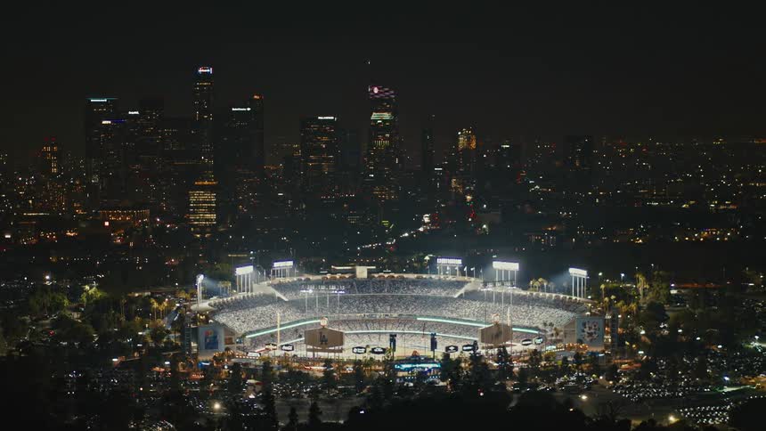 Fireworks go off in the sky around dodger stadium with the Los Angeles skyline behind