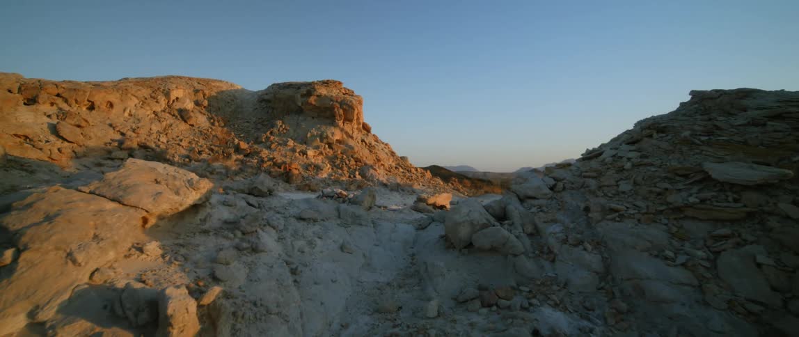Arid strip of sand passes between dirt hills toward mountains on the horizon