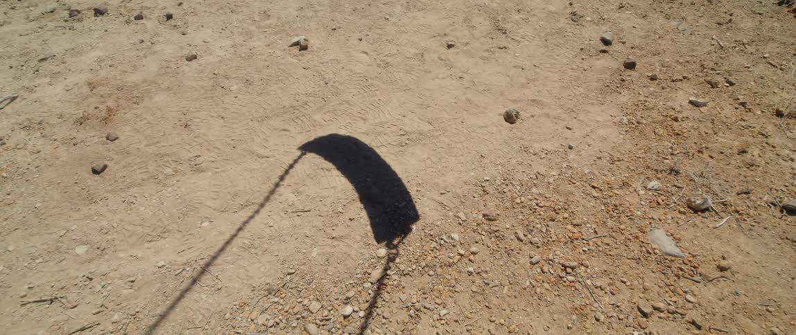 Shadow of swaying swing moves over bare dirt