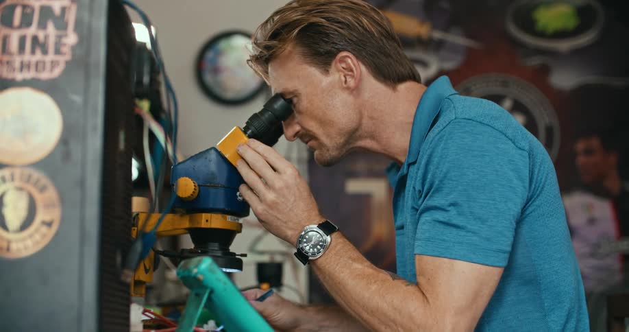 A man scrolls through his tablet and looks through a microscope