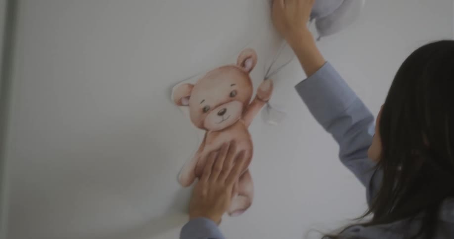 A woman is holding a cut out picture of a teddy bear against a wall