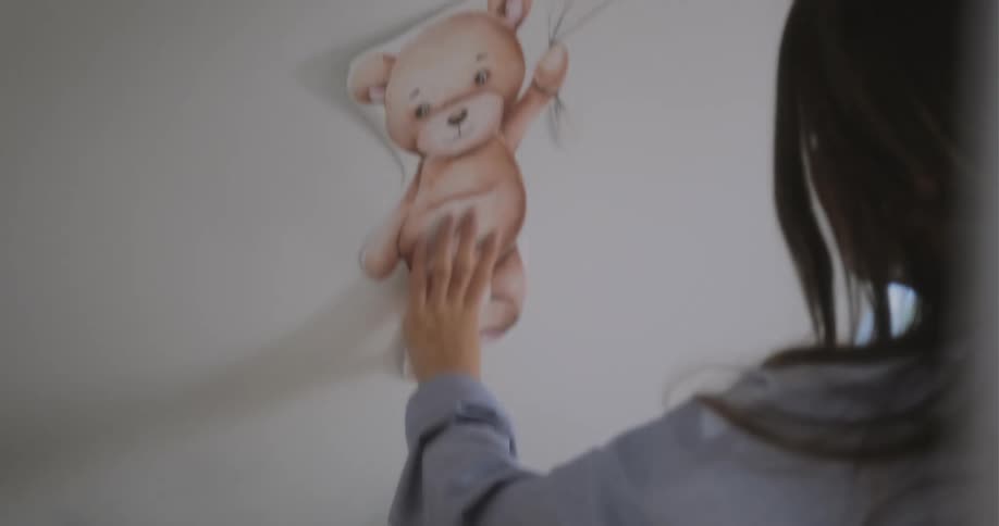 Pregnant woman with brown hair and blue shirt sticks decorations to wall in room