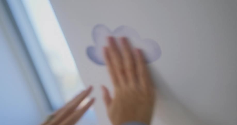 A woman is standing in a room rubbing her hands over picture of clouds she is putting on the walls