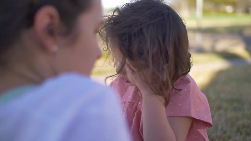A child eating a ring pop as she sits outside with a woman