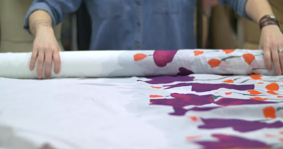 A woman rolls out some fabric from a roll