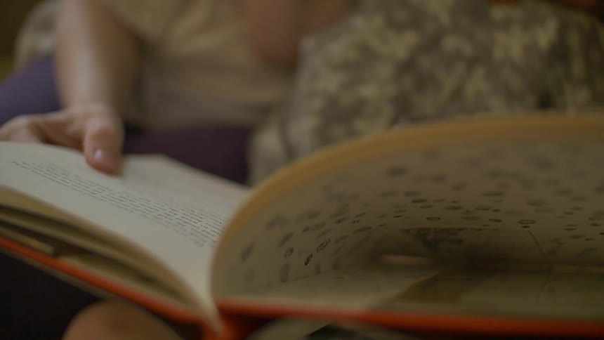 A woman's hand holding a book as she reads to a child