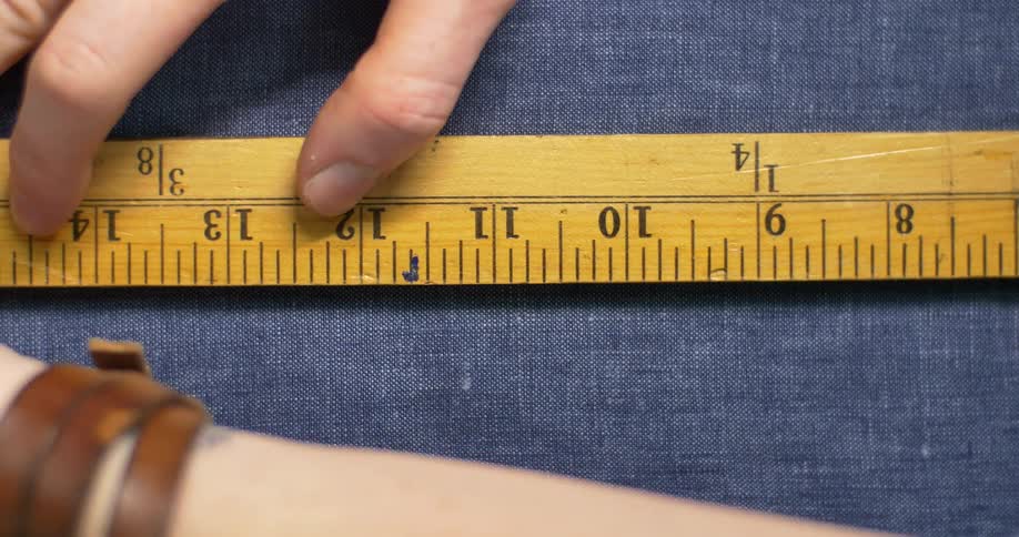 A ruler is used to mark a line across some fabric with a pencil