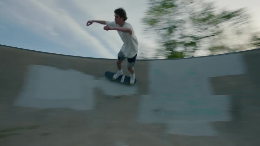 A teenage boy is riding his skateboard on concrete walls in a skateboard park