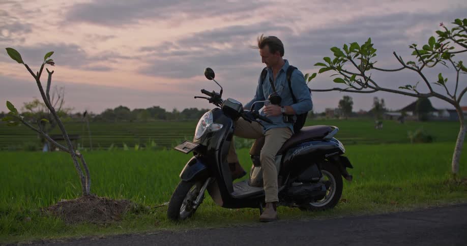 A man takes a picture on his cell phone then gets ready to start his moped